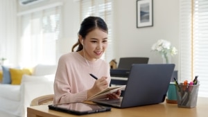 Young Asian woman uses a laptop and takes notes